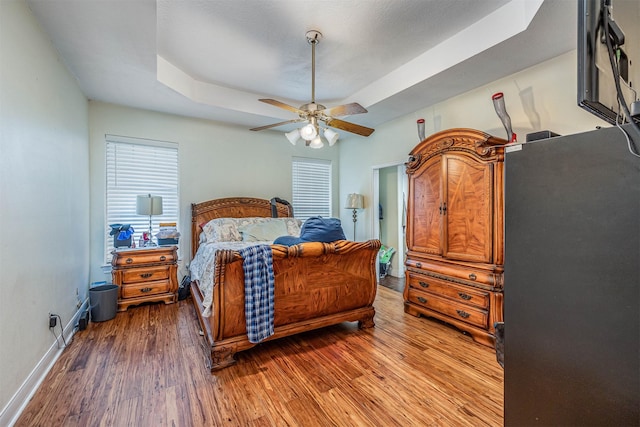 bedroom with wood-type flooring, a raised ceiling, and ceiling fan