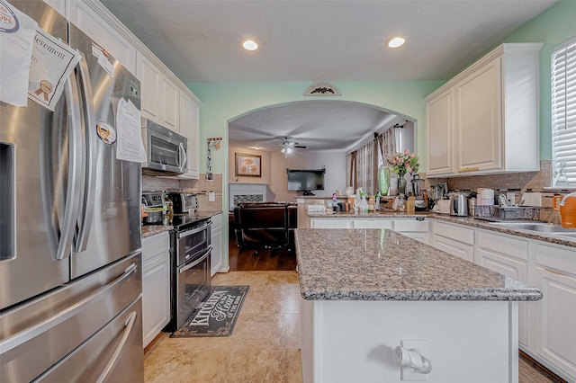 kitchen with white cabinetry, stone countertops, a center island, appliances with stainless steel finishes, and ceiling fan