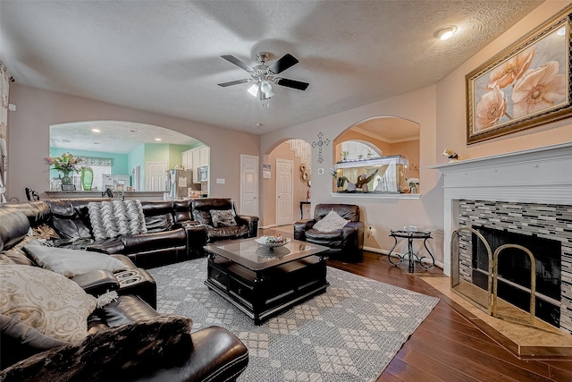 living room featuring ceiling fan, wood-type flooring, a tile fireplace, and a textured ceiling