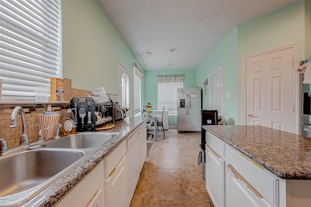 kitchen with sink, white cabinetry, stone countertops, stainless steel fridge with ice dispenser, and decorative backsplash