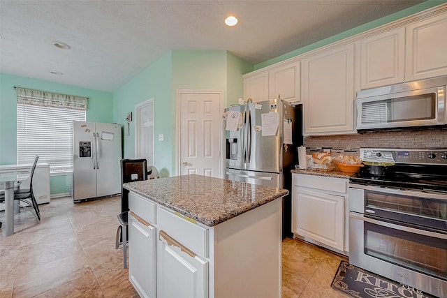 kitchen featuring stainless steel appliances, white cabinetry, a kitchen island, and stone counters