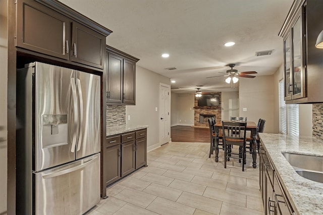 kitchen featuring light stone counters, stainless steel fridge with ice dispenser, decorative backsplash, and dark brown cabinets