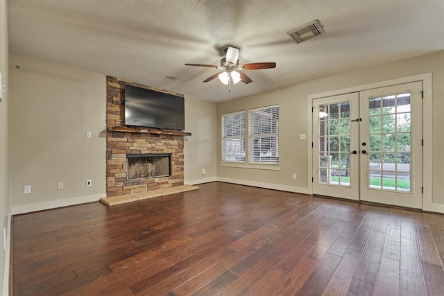 unfurnished living room featuring a stone fireplace, a textured ceiling, dark hardwood / wood-style flooring, and french doors