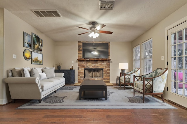 living room with ceiling fan, a stone fireplace, wood-type flooring, and a textured ceiling