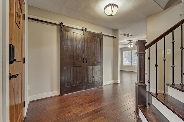 entrance foyer with a barn door, dark hardwood / wood-style floors, a textured ceiling, and ceiling fan