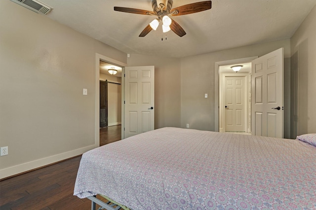 bedroom with a barn door, dark hardwood / wood-style floors, a textured ceiling, and ceiling fan