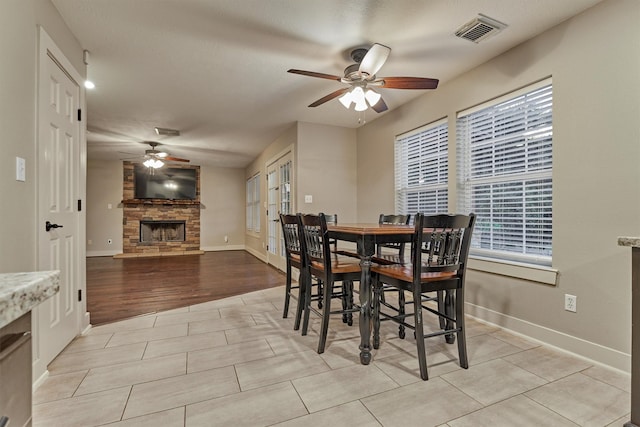 dining area with a stone fireplace, ceiling fan, and light wood-type flooring