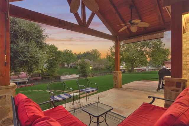 patio terrace at dusk with an outdoor living space, ceiling fan, and a lawn