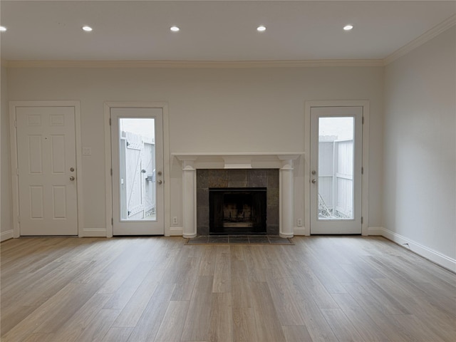 unfurnished living room featuring a tile fireplace, ornamental molding, and light wood-type flooring