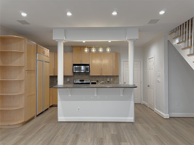 kitchen with light brown cabinets, stainless steel appliances, a kitchen breakfast bar, and ornate columns