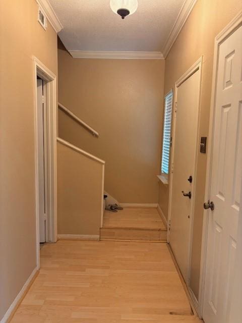 hallway with visible vents, baseboards, light wood-style flooring, and crown molding