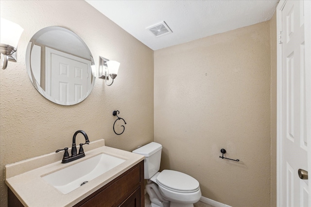 half bathroom featuring toilet, a textured wall, visible vents, and vanity