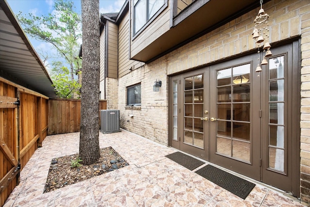 entrance to property featuring a patio, cooling unit, brick siding, fence, and french doors