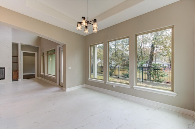 unfurnished dining area with a premium fireplace, a notable chandelier, and a tray ceiling