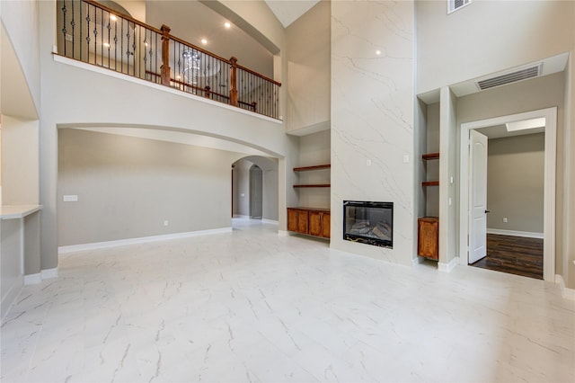 unfurnished living room with built in shelves, a high end fireplace, and a high ceiling