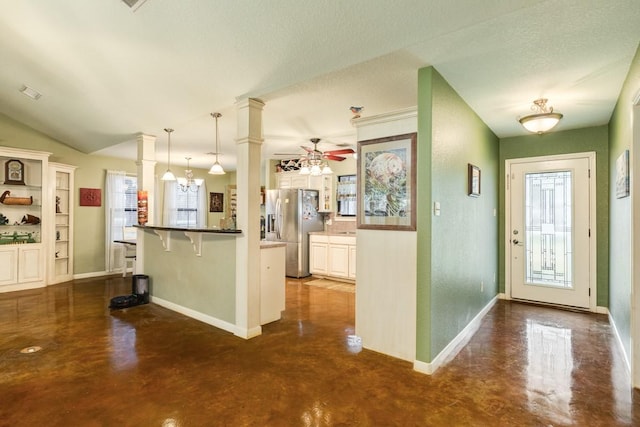 kitchen with decorative columns, decorative light fixtures, stainless steel fridge, a kitchen breakfast bar, and ceiling fan with notable chandelier