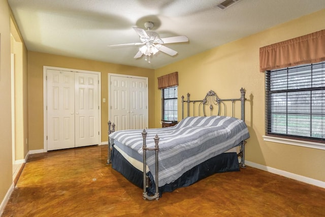 bedroom featuring two closets, concrete floors, and ceiling fan