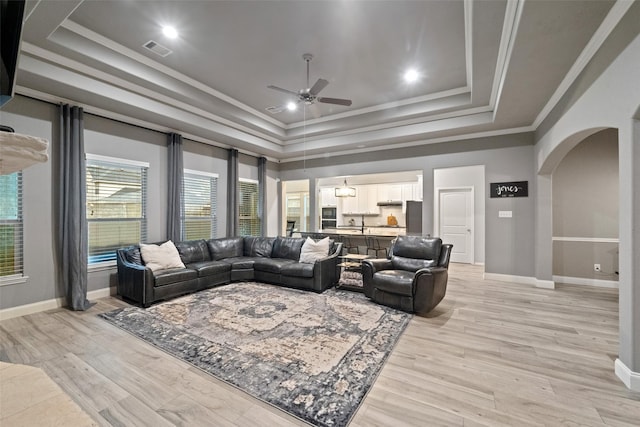 living room with visible vents, ornamental molding, arched walkways, a raised ceiling, and ceiling fan