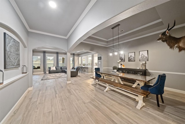 dining area with a raised ceiling, crown molding, and light wood-type flooring