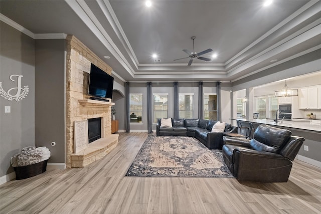 living room featuring crown molding, a fireplace, a tray ceiling, and light hardwood / wood-style flooring