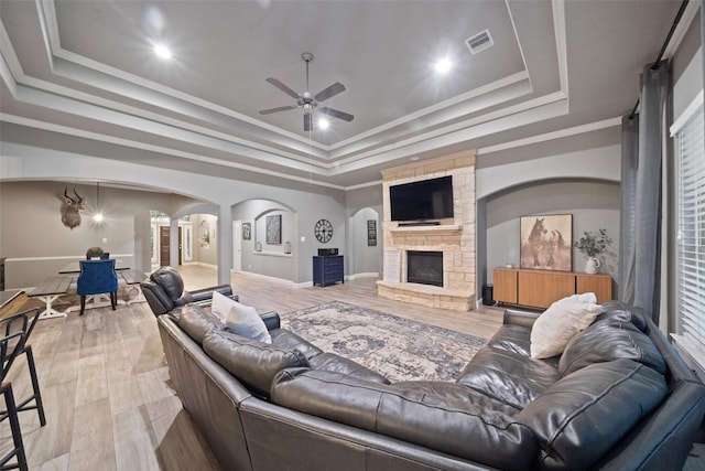 living room featuring a fireplace, ornamental molding, ceiling fan, a raised ceiling, and light hardwood / wood-style flooring