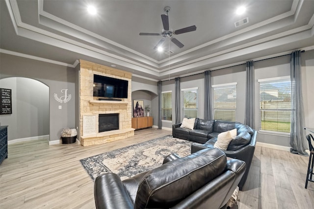 living room featuring light hardwood / wood-style floors, a stone fireplace, ornamental molding, and a raised ceiling