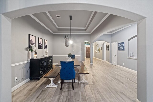 dining space with a tray ceiling, light hardwood / wood-style flooring, and ornamental molding