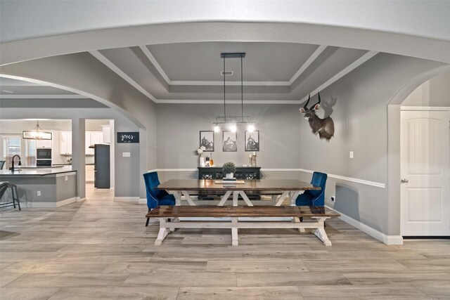 dining room with sink, a tray ceiling, ornamental molding, and light wood-type flooring