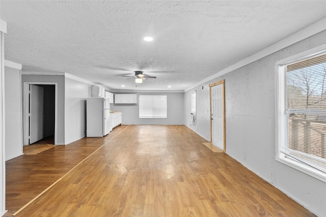 unfurnished living room with a textured ceiling, ornamental molding, ceiling fan, and light wood-type flooring