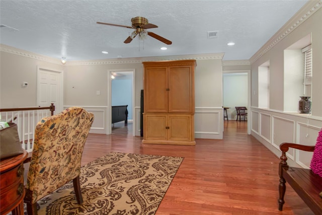 living area featuring crown molding, ceiling fan, a textured ceiling, and light hardwood / wood-style floors