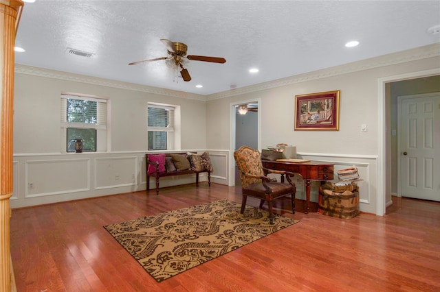 living area with crown molding, ceiling fan, hardwood / wood-style floors, and a textured ceiling