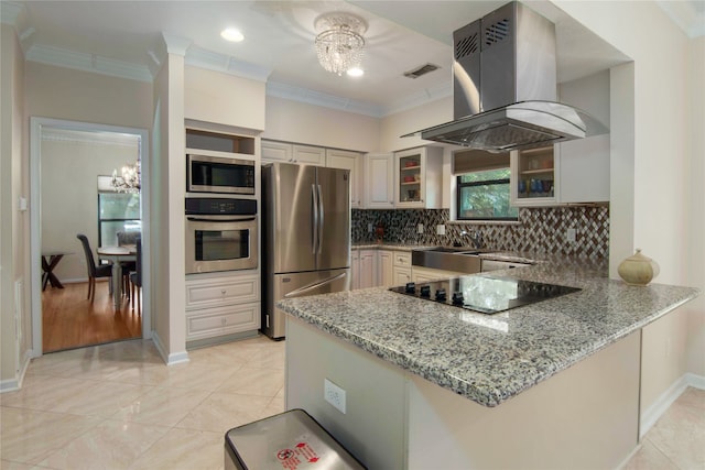 kitchen with appliances with stainless steel finishes, island range hood, kitchen peninsula, light stone countertops, and an inviting chandelier