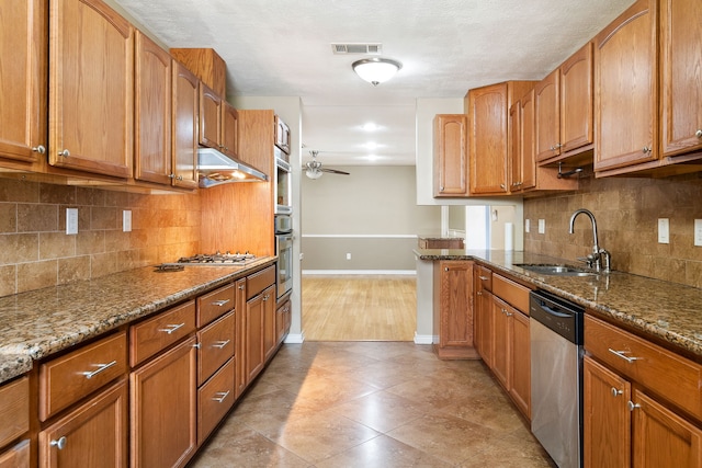 kitchen with sink, ceiling fan, stone counters, stainless steel appliances, and tasteful backsplash