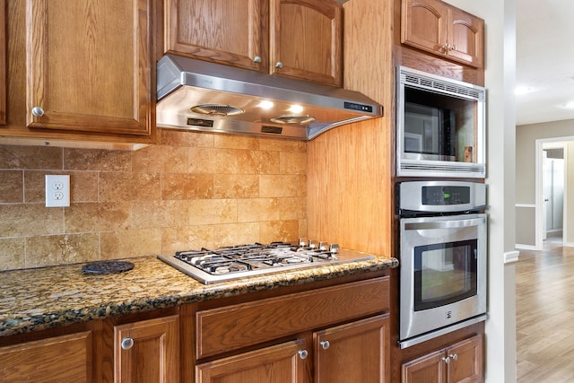 kitchen with hardwood / wood-style flooring, appliances with stainless steel finishes, decorative backsplash, and dark stone counters