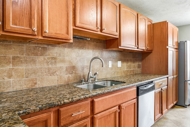 kitchen featuring sink, tasteful backsplash, a textured ceiling, dark stone countertops, and appliances with stainless steel finishes