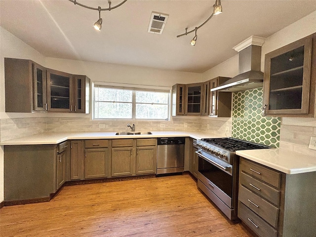 kitchen with appliances with stainless steel finishes, light hardwood / wood-style floors, sink, and wall chimney range hood