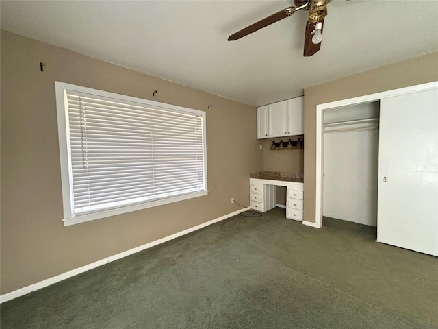 unfurnished bedroom with ceiling fan, built in desk, dark carpet, and a closet