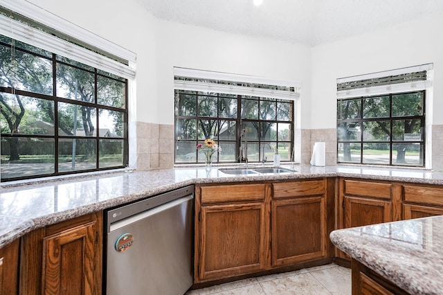 kitchen with light stone counters, stainless steel dishwasher, sink, and tasteful backsplash