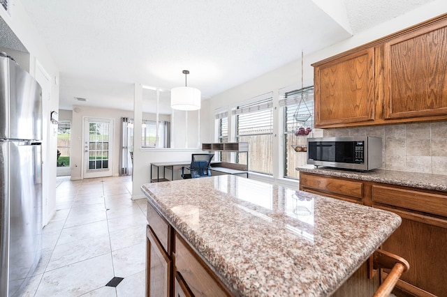 kitchen with pendant lighting, light tile patterned floors, appliances with stainless steel finishes, a center island, and tasteful backsplash