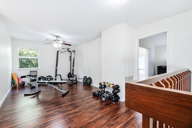 exercise room with dark wood-type flooring, ceiling fan, and a textured ceiling