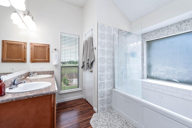 bathroom with vanity, wood-type flooring, a textured ceiling, vaulted ceiling, and tiled shower / bath