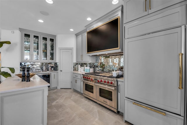 kitchen featuring gray cabinets, double oven range, range hood, decorative backsplash, and beverage cooler