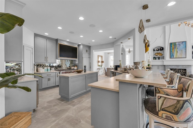 kitchen featuring gray cabinets, decorative light fixtures, backsplash, a kitchen breakfast bar, and kitchen peninsula