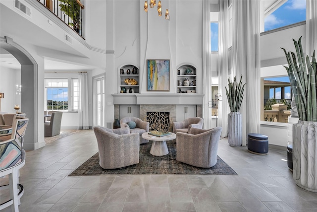 living room with a high ceiling, built in features, and a high end fireplace