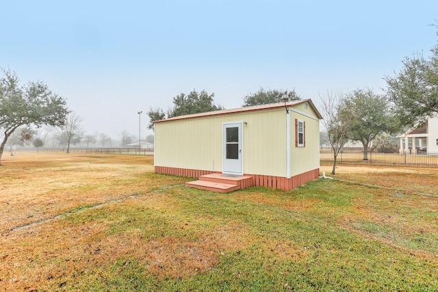 back of property with a rural view, an outbuilding, and a lawn