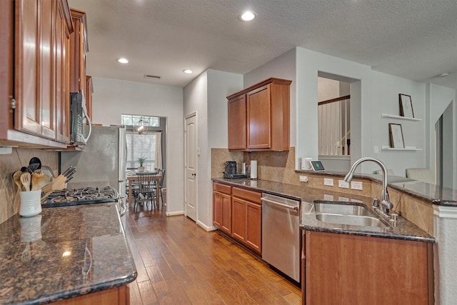 kitchen featuring sink, dark stone countertops, stainless steel appliances, kitchen peninsula, and light wood-type flooring