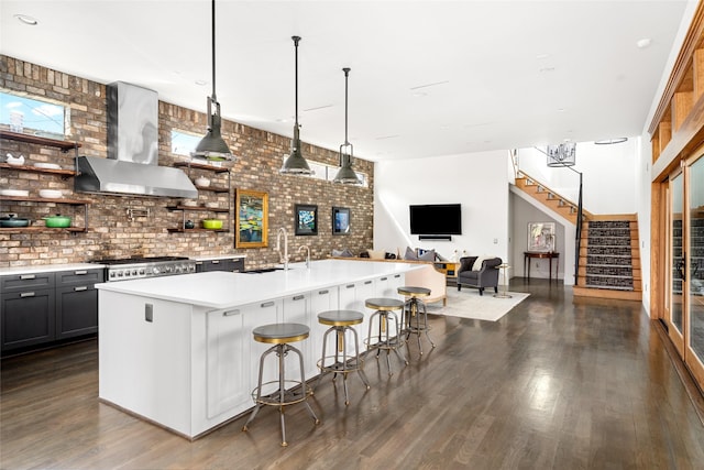 kitchen with a breakfast bar, sink, hanging light fixtures, wall chimney range hood, and a center island with sink