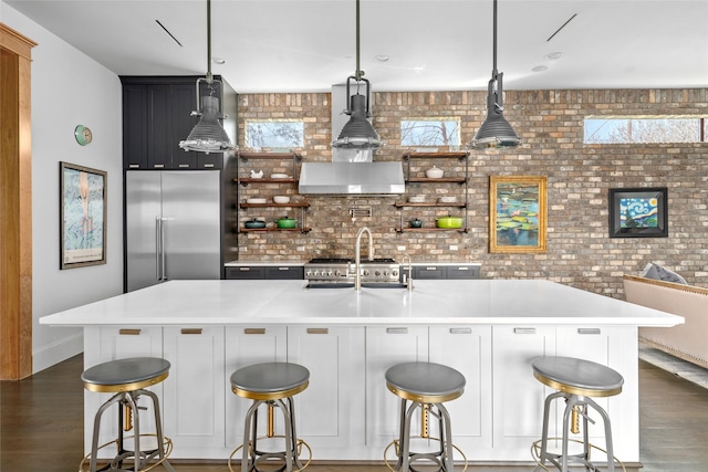 kitchen with a kitchen island with sink, hanging light fixtures, and stainless steel built in fridge