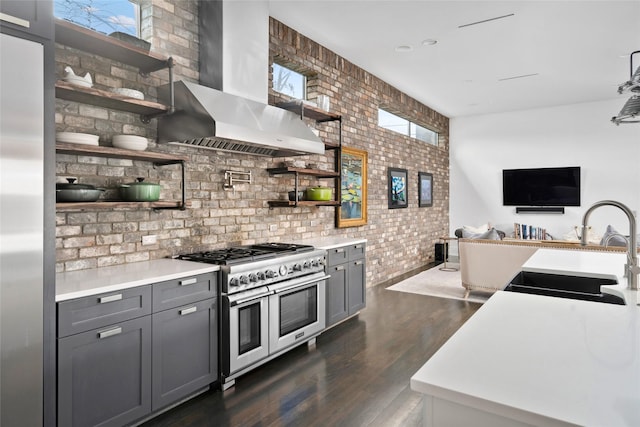 kitchen with gray cabinetry, sink, range with two ovens, and wall chimney range hood