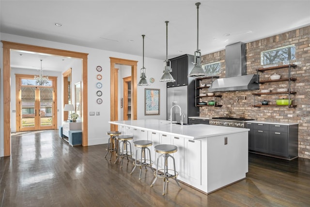 kitchen with pendant lighting, gray cabinetry, a kitchen breakfast bar, a center island with sink, and wall chimney exhaust hood